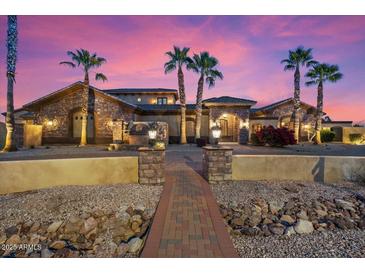 Twilight view of a stone accented home with a brick entry walk, desert landscaping, and mature palm trees at 5203 N 179Th Dr, Litchfield Park, AZ 85340