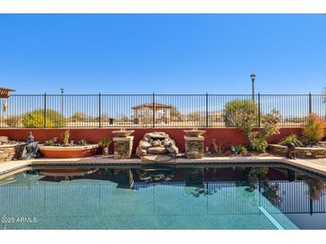 Beautiful pool featuring fountains, a rock waterfall, and a perimeter fence for added safety and style at 13849 S 179Th Ave, Goodyear, AZ 85338