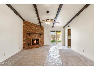 Spacious living room featuring a brick fireplace, exposed beam ceiling, and access to the backyard at 4312 W Paradise Dr, Glendale, AZ 85304