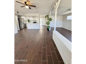 Spacious living room featuring wood-look tile floors, bright lighting, and an open-concept layout to the kitchen at 5729 N 64Th Dr, Glendale, AZ 85301