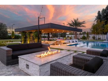 Luxurious outdoor living space with a fire pit, outdoor kitchen, and sparkling pool under a vibrant sunset sky at 10242 N 57Th St, Paradise Valley, AZ 85253