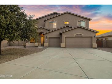 Spacious two-story home with a three-car garage and mature tree in the front yard with a colorful dusk sky backdrop at 21798 N Ingram Ct, Maricopa, AZ 85138