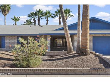 Charming single-story home featuring a brick facade, blue trim, desert landscaping, and mature palm trees at 402 E Muriel Dr, Phoenix, AZ 85022