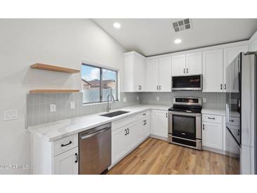 Bright kitchen featuring white cabinetry, modern appliances, marble counters, and light wood flooring at 13326 W Watson Ln, Surprise, AZ 85379