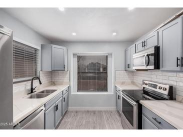 Updated kitchen featuring stainless steel appliances, gray cabinets, white subway tile, and light countertops at 8826 W Amelia Ave, Phoenix, AZ 85037