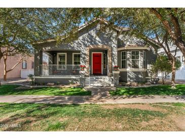 Charming home featuring a red front door, stone accents, covered porch, and lush green lawn at 3006 E Agritopia N Loop, Gilbert, AZ 85296