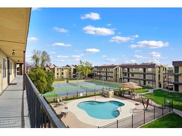 A view of the community pool, tennis courts, and grassy areas from an upper level balcony on a bright, sunny day at 461 W Holmes -- # 342, Mesa, AZ 85210