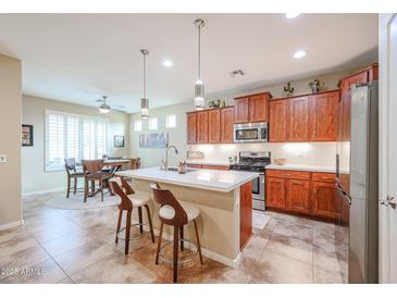 Well-lit kitchen featuring stainless steel appliances, tile floors, wooden cabinets and a breakfast bar at 17662 W Cedarwood Ln, Goodyear, AZ 85338
