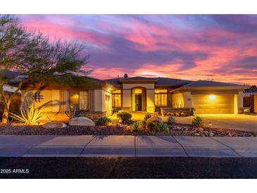 Inviting single-story home with desert landscaping, warm exterior lighting, and a colorful sunset sky at 2415 W Hazelhurst Ct, Anthem, AZ 85086