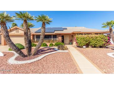 Charming home with a well-manicured front yard, complemented by palm trees and solar panels on the roof at 14718 W Ravenswood Dr, Sun City West, AZ 85375