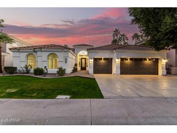 Beautiful home exterior with arched windows, tile roof, lush landscaping, and multi-car garage at sunset at 2043 E Clipper Ln, Gilbert, AZ 85234