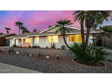 Charming single-story home with a desert landscape and mature palm trees under a beautiful sunset sky at 10846 W Crosby Dr, Sun City, AZ 85351