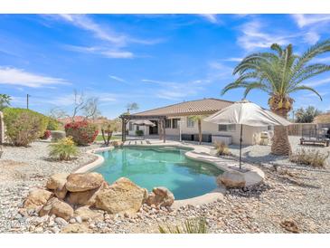 Backyard pool featuring a rock waterfall, pergola, and lush landscaping under a clear blue sky at 14612 W Edgemont Ave, Goodyear, AZ 85395