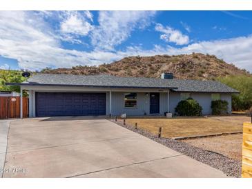 Single-story home featuring a two-car garage, desert landscaping, and a mountain in the background under a cloudy, blue sky at 9005 E Grandview Dr, Mesa, AZ 85207