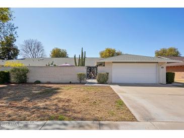 Charming single-story home featuring a brick wall, gate, desert landscaping, and a two-car garage at 18614 N Conestoga Dr, Sun City, AZ 85373