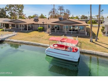 Waterfront home featuring a boat dock and a red and white pontoon boat on a canal at 10116 W Bolivar Dr, Sun City, AZ 85351