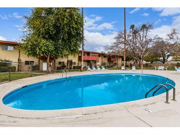 Outdoor pool with lounge chairs and grassy area in front of building on a bright sunny day at 355 E Thomas Rd # B110, Phoenix, AZ 85012