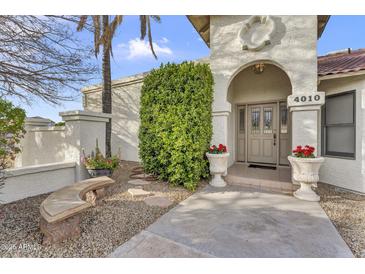 Inviting front entrance with decorative planters and a stone bench, framed by a lush green shrub and stucco walls at 4010 E Grandview St, Mesa, AZ 85205