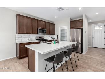 Modern kitchen features brown cabinets, stainless steel appliances, white countertops, and wood floors at 10983 W Mckinley St, Avondale, AZ 85323