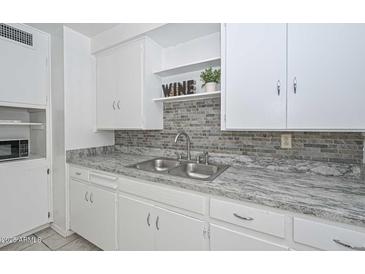 Kitchen featuring granite counters, grey brick backsplash, and stainless steel sink at 11223 W Missouri Ave, Youngtown, AZ 85363