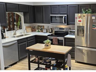 Well-lit kitchen with stainless steel appliances, dark cabinets, light countertops, and a mobile island at 855 E Vaughn Ave, Gilbert, AZ 85234