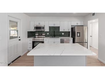 Modern kitchen features white cabinets, stainless steel appliances, and a striking dark green tile backsplash at 10815 W Crosby Dr, Sun City, AZ 85351