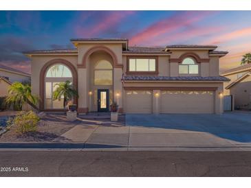 A grand home with a three-car garage and arched windows, complemented by desert landscaping and palm trees at 12925 W Llano Dr, Litchfield Park, AZ 85340