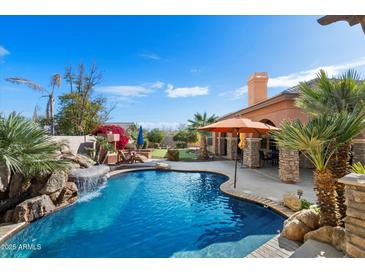 Stunning pool featuring a rock waterfall, lush landscaping, and patio seating, perfect for outdoor relaxation at 3132 E Harwell Rd, Phoenix, AZ 85042