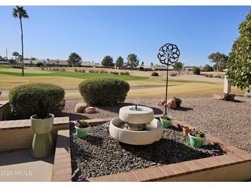 Relaxing backyard retreat featuring a stone fountain, colorful flowers, and well-manicured landscaping overlooking the green golf course at 5902 S Amberwood Dr, Sun Lakes, AZ 85248