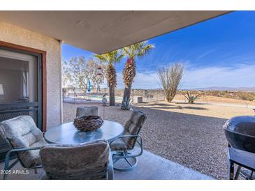 Outdoor patio area with a table and chairs with gravel, plants, and swimming pool in the background at 100 N Vulture Mine Rd # 103, Wickenburg, AZ 85390