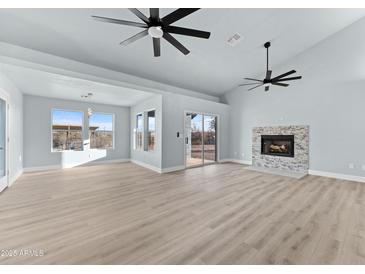 Bright living room featuring light wood floors, a stone fireplace, large windows and sliding glass door to the backyard at 1100 W Palo Verde Dr, Wickenburg, AZ 85390