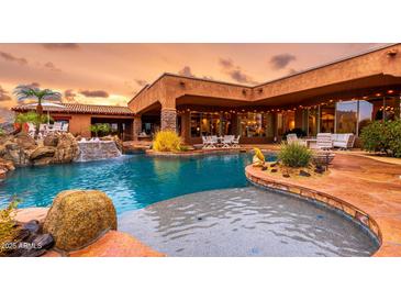 Stunning pool with rock waterfall features and lush landscaping, perfect for outdoor relaxation and entertainment at 12160 E Whispering Wind Dr, Scottsdale, AZ 85255