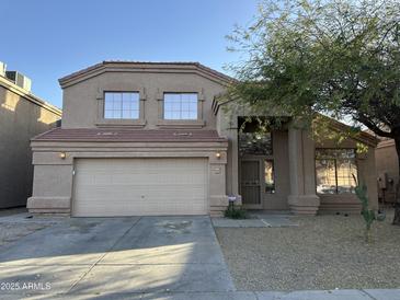 Two-story home featuring a two-car garage, desert landscaping, and a tree in the front yard at 12733 W Boca Raton Rd, El Mirage, AZ 85335