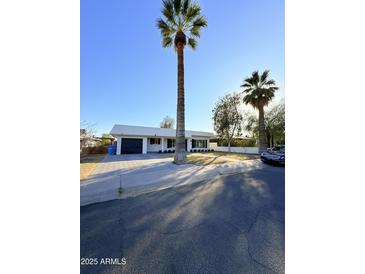 Charming home featuring a large palm tree, manicured lawn, and a driveway leading to an attached garage at 1837 W Virginia Ave, Phoenix, AZ 85007