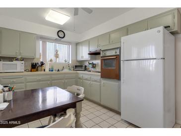 Traditional kitchen featuring gray cabinets, tile countertops, white appliances, and an adjacent dining area at 10408 N 105Th Ave, Sun City, AZ 85351