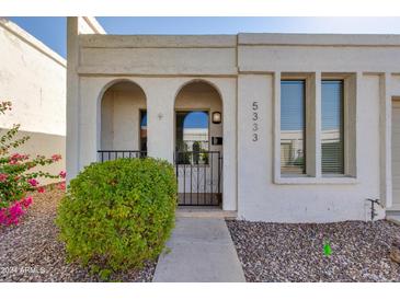 Charming stucco home featuring an arched entryway, wrought iron gate, and well-maintained landscaping at 5333 N Las Casitas Pl, Phoenix, AZ 85016