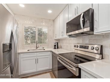 Modern kitchen with stainless steel appliances, white cabinets, tile backsplash, and a bright window at 19400 N Westbrook Pkwy # 241, Peoria, AZ 85382