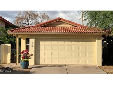 Attached garage with a red tile roof, a concrete driveway, and a blue planter with red flowers at 4335 E Monte Way, Phoenix, AZ 85044