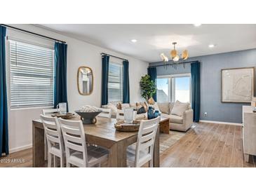 Elegant living room with hardwood floors, modern chandelier, and large windows with blue curtains at 23997 W Cocopah St, Buckeye, AZ 85326