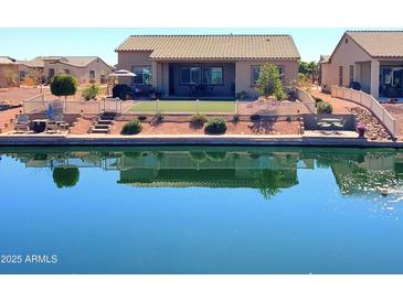 A beautiful waterfront home features a covered patio, a fenced yard, and views of the sparkling water at 42024 W Rosewood Ln, Maricopa, AZ 85138