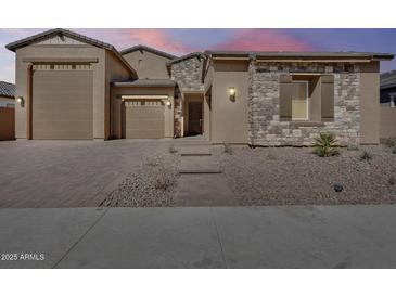 Charming single-story home featuring a stone facade, desert landscaping, and a three-car garage at 7694 W Desert Spoon Dr, Peoria, AZ 85383