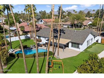 Aerial view of the property featuring a sparkling pool, play area, lush landscaping, and a covered patio at 10052 N 77Th St, Scottsdale, AZ 85258
