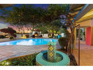 Inviting backyard oasis featuring a sparkling pool, decorative water feature, and cozy outdoor fireplace at twilight at 7451 E Long Rifle Rd, Carefree, AZ 85377