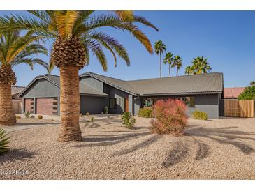 Charming desert home featuring a gray exterior, two-car garage and low maintenance landscape with mature palm trees at 5726 E Woodridge Dr, Scottsdale, AZ 85254