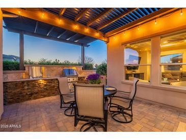 Inviting outdoor kitchen with stainless steel grill, stone counter, and cozy seating under a pergola with string lights at 706 E La Palta St, Queen Creek, AZ 85140