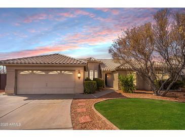 Charming single-story home with a tile roof, lush landscaping, and a two-car garage, bathed in the warm light of sunset at 750 S Cholla St, Gilbert, AZ 85233
