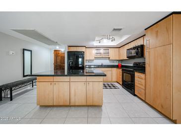 Bright kitchen with stainless steel appliances, tile floors, light wood cabinets, and a black island at 7860 E Camelback Rd # 309, Scottsdale, AZ 85251