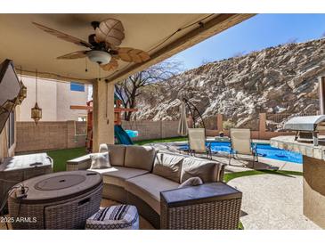 Inviting covered patio with stylish seating and outdoor kitchen, overlooking a pool and picturesque rock wall backdrop at 16834 S 20Th Pl, Phoenix, AZ 85048