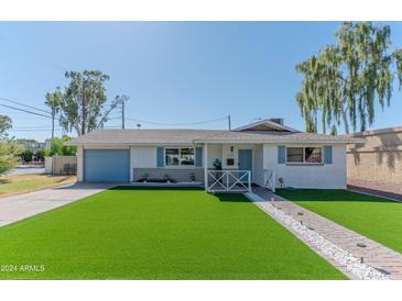 Charming single-story home featuring a manicured front yard, blue shutters, and a light blue garage door at 1749 E Medlock Dr, Phoenix, AZ 85016