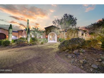 Desert home exterior with landscaped front yard, stone facade, and a paver driveway at sunset at 14371 E Kalil Dr, Scottsdale, AZ 85259